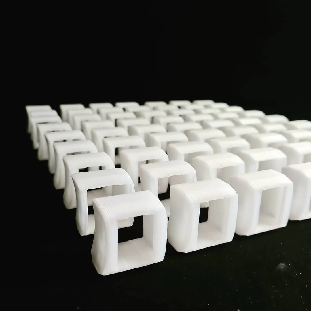 Mini serija istovetnih belih 3D odštampanih rezervnih delova poređanih u redove na crnoj podlozi